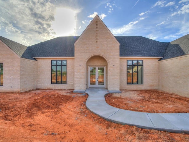 view of exterior entry with brick siding, french doors, and roof with shingles