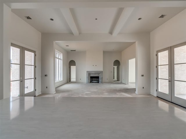 unfurnished living room featuring beamed ceiling, arched walkways, baseboards, and french doors