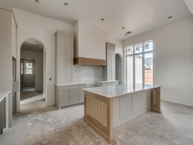 kitchen with decorative backsplash, visible vents, arched walkways, and unfinished concrete flooring