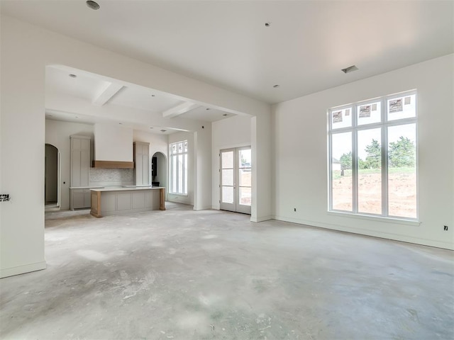 unfurnished living room with coffered ceiling, visible vents, arched walkways, beamed ceiling, and concrete floors