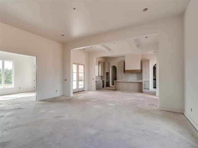 unfurnished living room featuring arched walkways, concrete floors, baseboards, and french doors