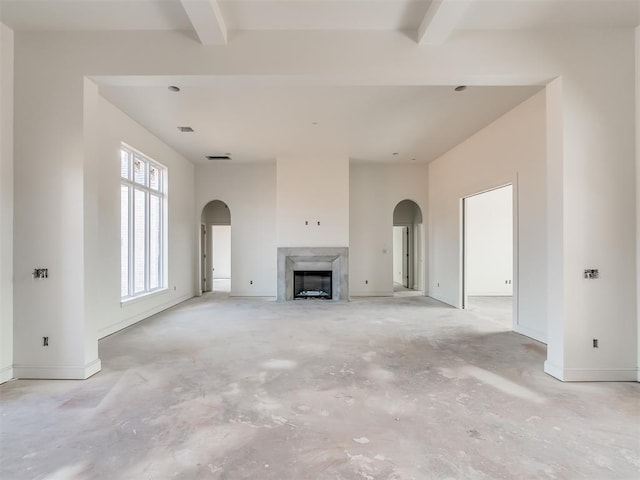 unfurnished living room featuring beamed ceiling, arched walkways, and unfinished concrete flooring