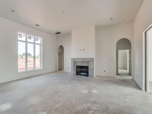 unfurnished living room featuring arched walkways, a high end fireplace, visible vents, and unfinished concrete floors