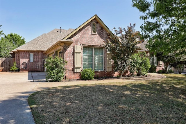 view of front of home featuring a front lawn, fence, a patio, brick siding, and roof with shingles