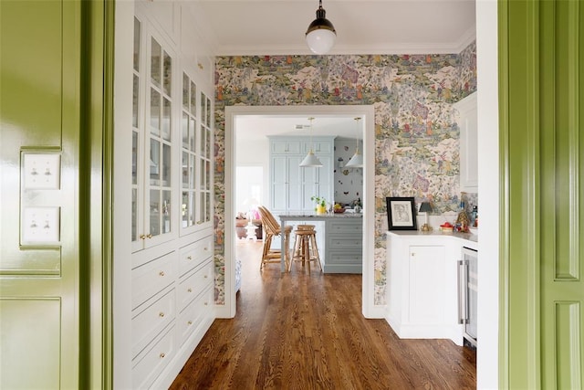 corridor featuring crown molding, beverage cooler, wallpapered walls, and dark wood finished floors