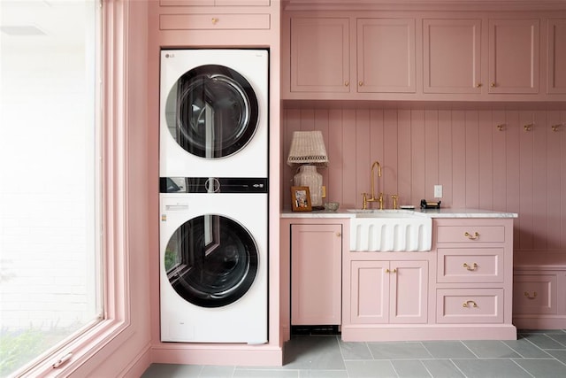 clothes washing area featuring cabinet space, stacked washer and dryer, and a sink