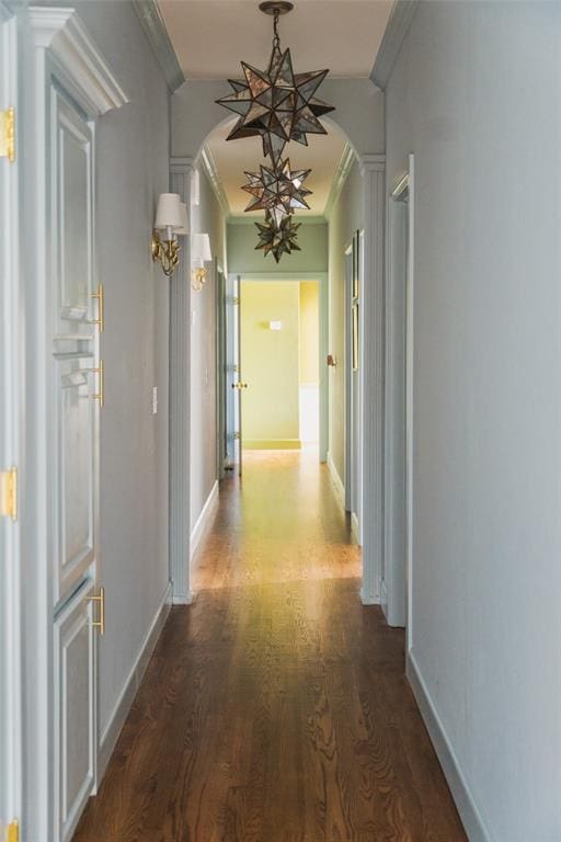 corridor featuring crown molding, an inviting chandelier, arched walkways, dark wood finished floors, and baseboards
