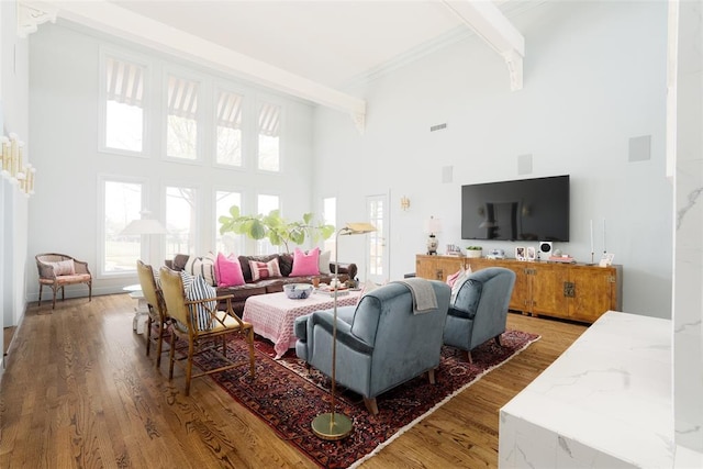 living area featuring visible vents, crown molding, light wood-type flooring, beamed ceiling, and a high ceiling