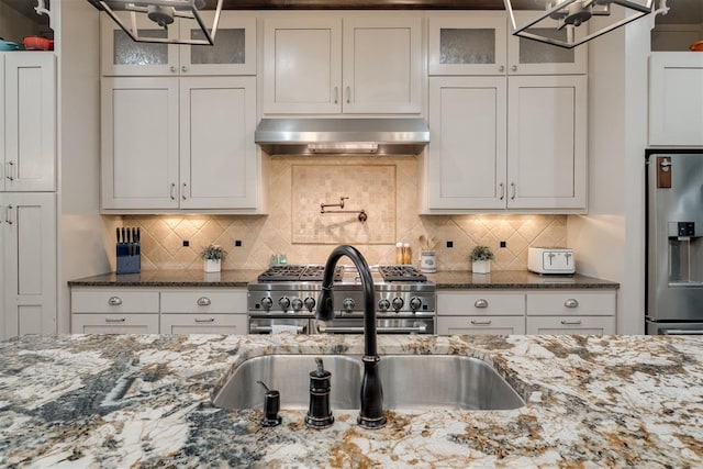 4301 Frisco Bridge Blvd, Edmond, OK 73034 - kitchen with under cabinet range hood, stainless steel appliances, glass insert cabinets, and dark stone counters