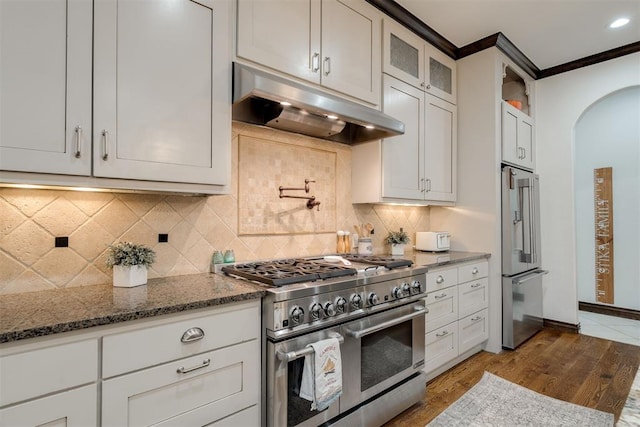 4301 Frisco Bridge Blvd, Edmond, OK 73034 - kitchen featuring premium appliances, under cabinet range hood, arched walkways, dark stone countertops, and wood finished floors