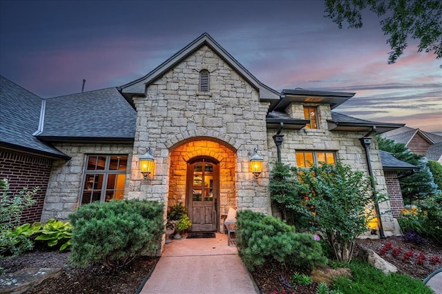 4400 The Ranch Rd, Edmond, OK 73034 - exterior entry at dusk with stone siding and a shingled roof