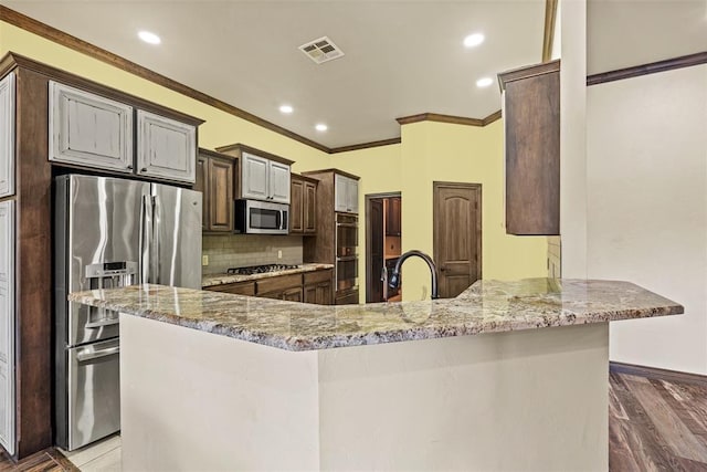212 SW 144th, Oklahoma City, OK 73170 - kitchen featuring stainless steel appliances, light stone counters, ornamental molding, backsplash, and a peninsula