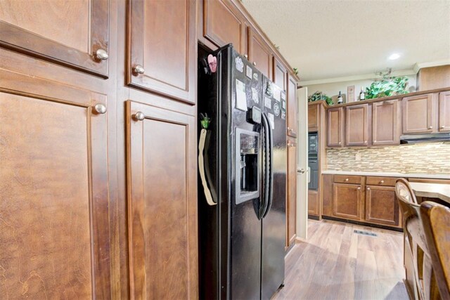 kitchen with tasteful backsplash, ornamental molding, black fridge, under cabinet range hood, and light wood-style flooring
