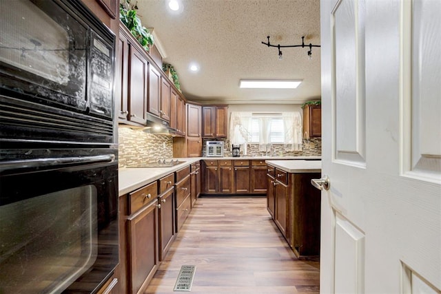 kitchen featuring decorative backsplash, light countertops, a textured ceiling, light wood finished floors, and black appliances