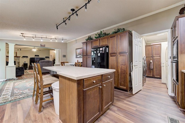 kitchen featuring crown molding, a breakfast bar area, a center island, light wood finished floors, and black appliances