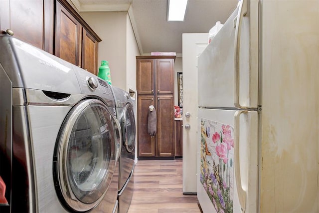 laundry area featuring crown molding, light wood-style flooring, cabinet space, and washing machine and clothes dryer