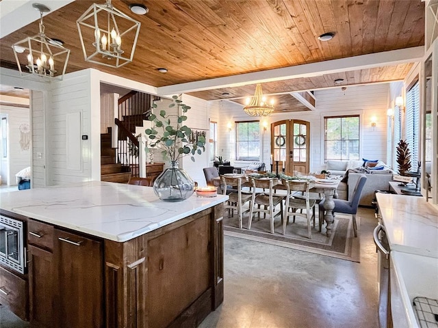 kitchen featuring an inviting chandelier, finished concrete flooring, open floor plan, stainless steel microwave, and wooden ceiling