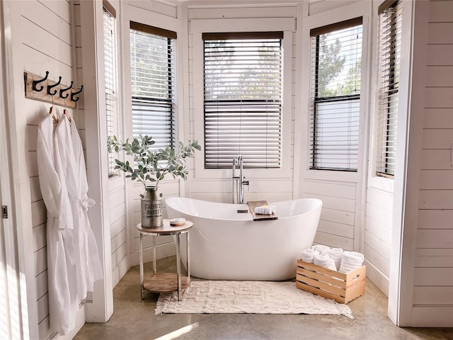 full bathroom featuring a soaking tub, a wealth of natural light, and finished concrete flooring