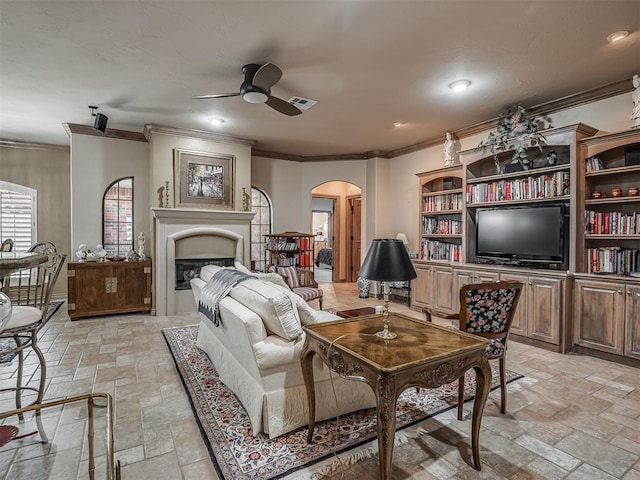 12304 N St Lukes Ln, Oklahoma City, OK 73142 - living area with crown molding, a ceiling fan, stone tile floors, arched walkways, and a fireplace