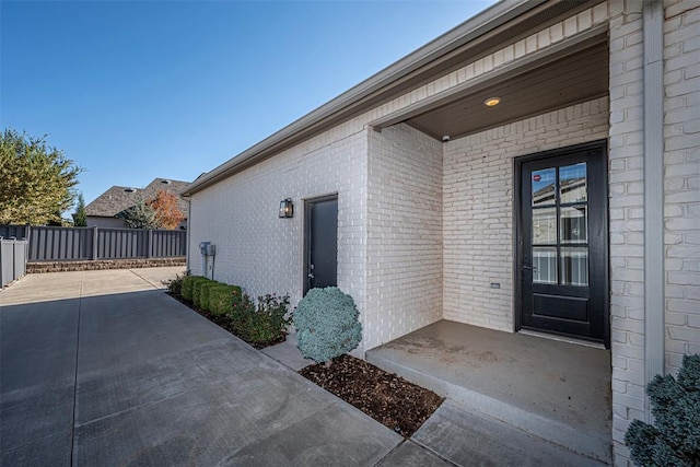 view of exterior entry with fence, a patio area, and brick siding