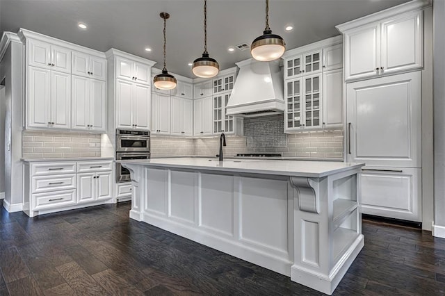 kitchen with recessed lighting, a kitchen island with sink, light countertops, white cabinetry, and premium range hood