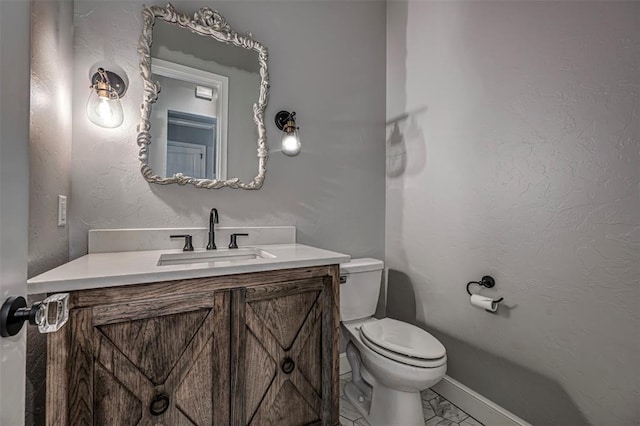 half bathroom with baseboards, marble finish floor, toilet, and vanity