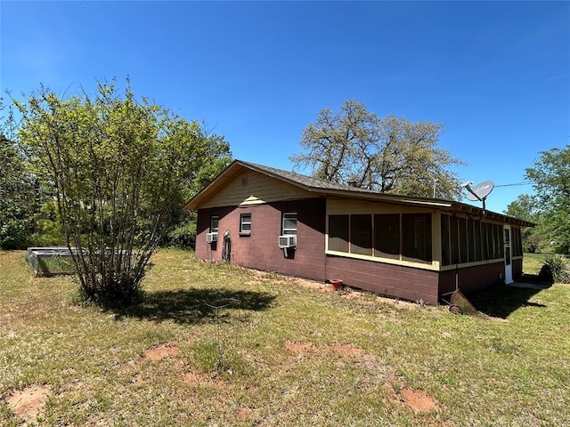 view of side of home with cooling unit, concrete block siding, a sunroom, and a lawn