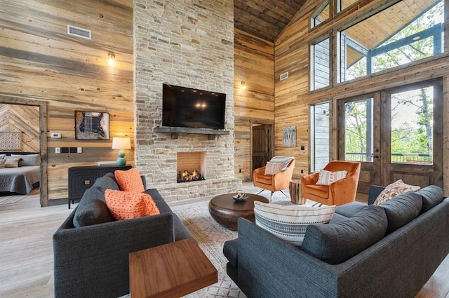 living area with wooden walls, a stone fireplace, wood ceiling, and high vaulted ceiling