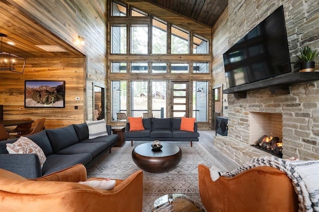 living area featuring wooden walls, a notable chandelier, wooden ceiling, a stone fireplace, and high vaulted ceiling