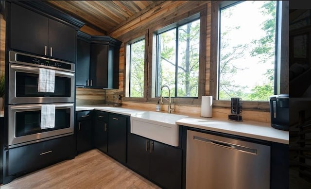 kitchen featuring stainless steel appliances, light countertops, wooden ceiling, dark cabinetry, and a sink