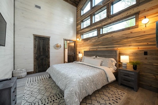 bedroom featuring hardwood / wood-style floors, multiple windows, a towering ceiling, wood walls, and visible vents