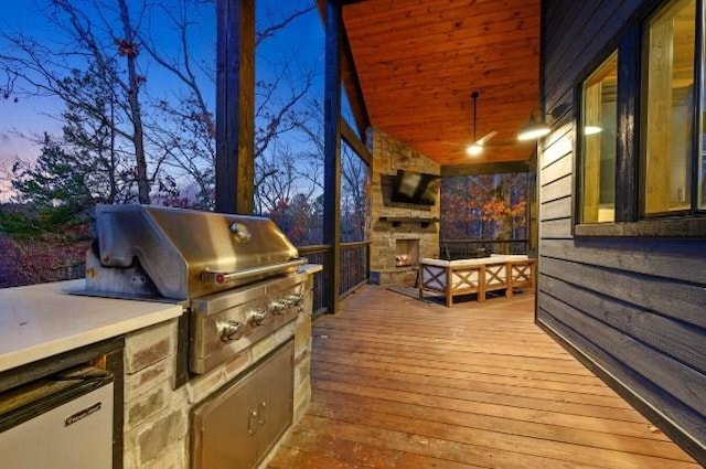 deck with a grill, an outdoor stone fireplace, and exterior kitchen