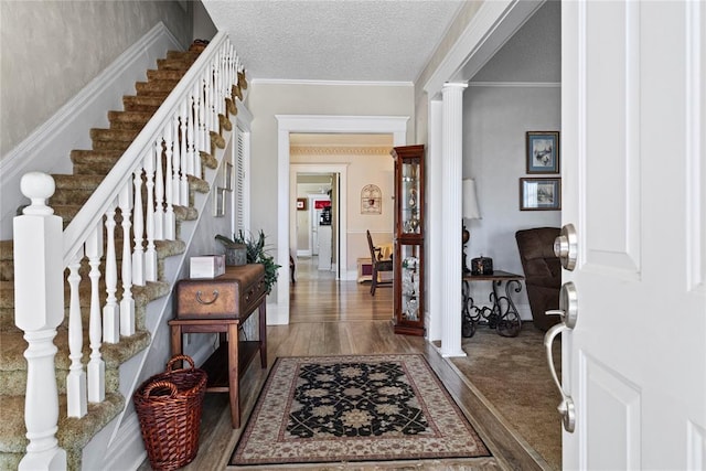 entrance foyer featuring stairway, a textured ceiling, crown molding, and wood finished floors