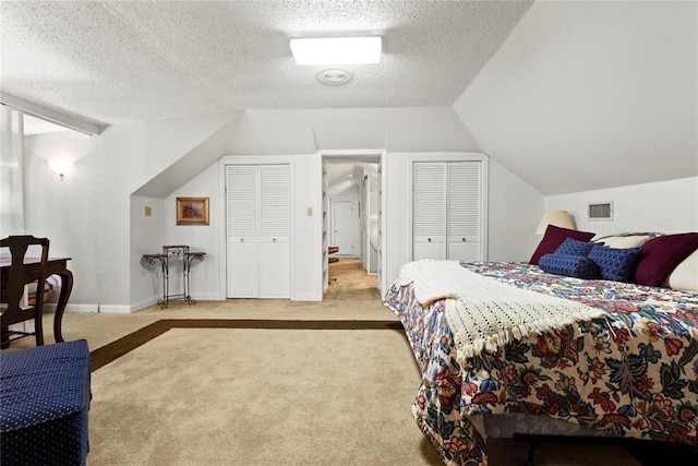 bedroom featuring carpet flooring, a textured ceiling, visible vents, lofted ceiling, and multiple closets