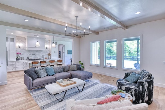 living room with light wood-style flooring, visible vents, beam ceiling, and baseboards