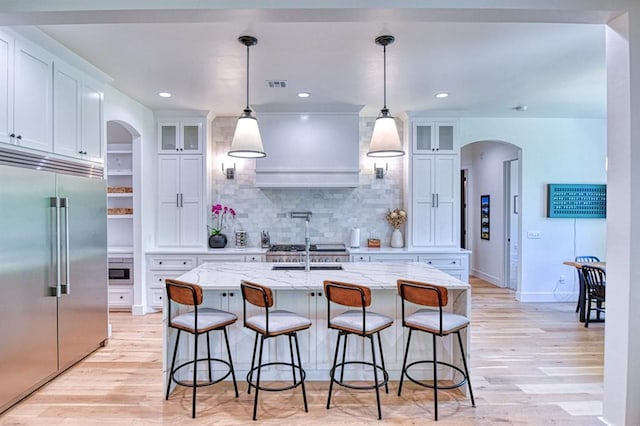 kitchen with built in fridge, arched walkways, visible vents, and light wood-type flooring