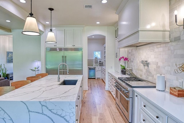 kitchen with a sink, premium appliances, backsplash, premium range hood, and arched walkways