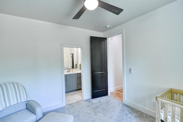 bedroom featuring a sink, ceiling fan, light carpet, baseboards, and ensuite bathroom