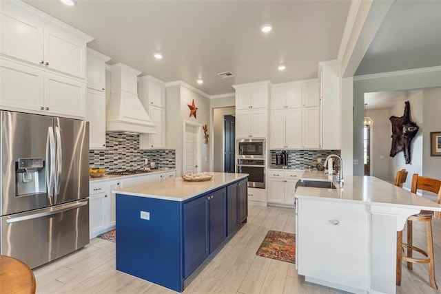 kitchen with appliances with stainless steel finishes, blue cabinetry, a sink, custom range hood, and decorative backsplash