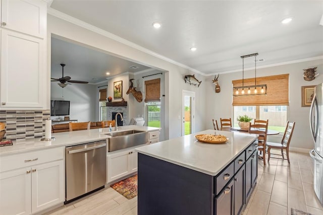 kitchen with a sink, appliances with stainless steel finishes, a stone fireplace, decorative backsplash, and white cabinetry