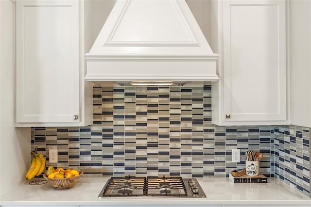 detailed view of stainless steel gas stovetop, decorative backsplash, light countertops, and white cabinetry
