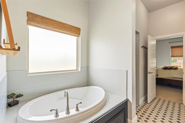 bathroom with ensuite bathroom, a bath, and baseboards