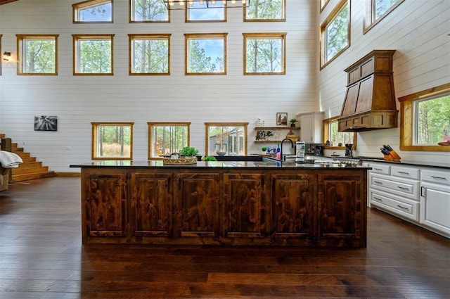 kitchen featuring a towering ceiling, dark countertops, white cabinets, wooden walls, and dark wood-type flooring