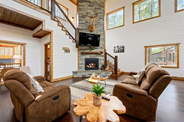 living area with wooden walls, a high ceiling, a stone fireplace, and wood-type flooring