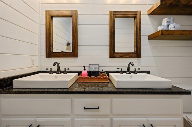 bathroom with wooden walls, double vanity, and a sink