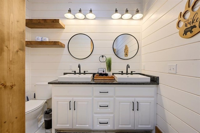 bathroom featuring double vanity, a sink, wooden walls, and toilet