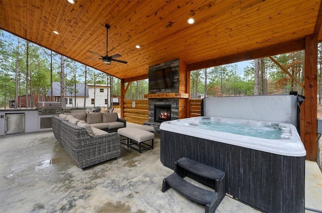 view of patio / terrace featuring an outdoor living space with a fireplace, a hot tub, exterior kitchen, ceiling fan, and area for grilling