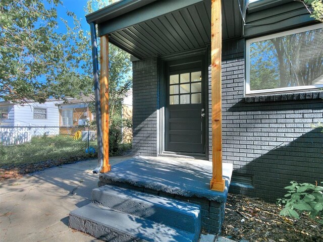 entrance to property featuring brick siding, a patio area, and fence