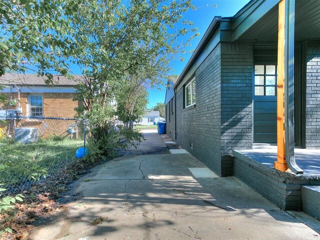 view of side of home with brick siding, fence, a patio, and driveway