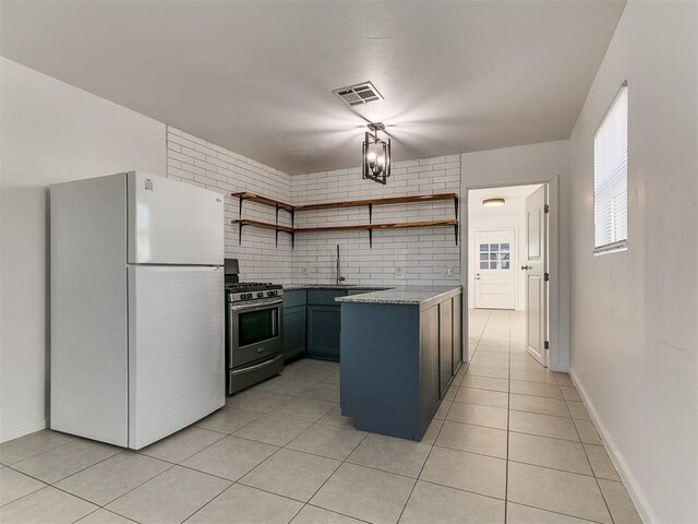 kitchen featuring stainless steel gas stove, open shelves, visible vents, light tile patterned floors, and freestanding refrigerator